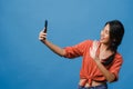 Smiling adorable Asian female making selfie photo on smart phone with positive expression in casual clothing and stand isolated on Royalty Free Stock Photo