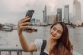 Smiling adorable Asian female making selfie photo on smartphone and Ho Chi Minh city with Bitexco Financial Tower, many buildings