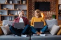 Smiling adult caucasian husband look at wife with laptop in living room interior in evening. Work and study