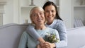 Smiling adult daughter congratulate mature mom presenting flowers