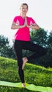 Smiling adult female in pink T-shirt is staying and practising meditation