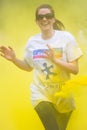 Smiling adult female runner wearing sunglasses runs through thrown yellow paint on a charity colour paint run.