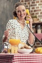 smiling adult housewife holding jug of orange juice talking by vintage wired phone Royalty Free Stock Photo