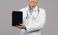 Smiling adult japanese guy therapist in white coat with stethoscope shows tablet with empty screen