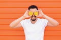 Smiling adult man with beard and moustache in white shirt pose standing against against wall covering eyes with two sliced oranges Royalty Free Stock Photo