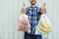 Smiling adult man holding reusable eco bags with fresh fruits and showing LIKE sign. Zero waste shopping, ban single use plastic Royalty Free Stock Photo