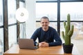 Smiling adult man looking in camera while sitting at desk with laptop. Royalty Free Stock Photo