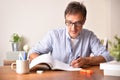 Smiling adult man tudying on wooden table underlining in book