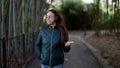 A smiling adult woman with headphones listens to music and dances amusingly in a city park. Modern urban lifestyle and