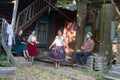 A smiling adult woman in colorful skirt dancing by the music near the country house - a man playing balalaika sitting on