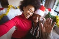 Smiling african american adult daughter and senior mother in santa hats taking christmas selfie Royalty Free Stock Photo