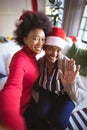 Smiling african american adult daughter and senior mother in santa hats taking christmas selfie Royalty Free Stock Photo