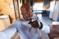 Smiling african american bald senior man pointing towards camera while taking selfie in log cabin Royalty Free Stock Photo