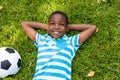 Smiling african american boy lying with hands behind head by soccer ball on grass in backyard Royalty Free Stock Photo