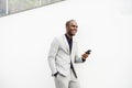 Smiling African American business man leaning against white wall with mobile phone Royalty Free Stock Photo