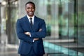 Smiling african american businessman CEO standing proud with arms crossed outside office workplace, colorful, reflective glass bui Royalty Free Stock Photo