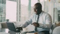 Smiling African American businessman in formal clothes paying online bill using his credit card and laptop in Royalty Free Stock Photo