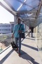 Smiling african american businessman with luggage walking ahead of businesswoman at airport corridor Royalty Free Stock Photo