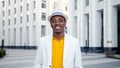 Smiling African American businessman in white fedora hat with blue strip walks along city square