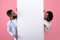 Smiling African American couple looking at empty advertising banner with space for design over pink studio background Royalty Free Stock Photo