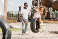 smiling african american father standing near daughter on tire swing