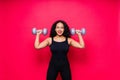 Smiling african american female doing hand exercises with dumbbells on red studio background.