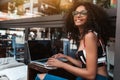 Smiling African-American female employer in eyeglasses with a laptop in an outdoor cafe; cheerful Brazilian businesswoman with