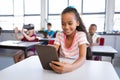 Smiling african american girl using digital tablet while sitting on her desk in class at school Royalty Free Stock Photo