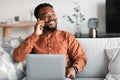 Smiling African American Guy Using Laptop Talking On Phone Indoors Royalty Free Stock Photo