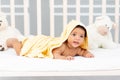 Smiling African-American little baby lies in bed after a bath in a yellow towel