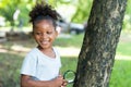 Smiling African American little girl has fun holding magnifying glass to explore and look bugs on the tree between learning beyond