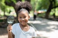 Smiling African American little girl has fun holding magnifying glass to explore and look bugs on the tree between learning beyond