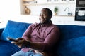 Cheerful and happy African-American man with dreadlocks holding TV remote controller Royalty Free Stock Photo