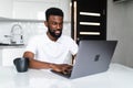 Smiling african american man drinking coffee and using laptop on the kitchen Royalty Free Stock Photo