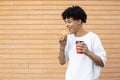 Smiling African-American man holding a cup of coffee and biting into an orange donut Royalty Free Stock Photo