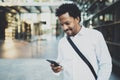 Smiling African American man holding mobile phone in hands and checking email.Blurred background. Royalty Free Stock Photo