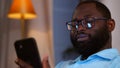 Smiling african american man holding smartphone using social media apps sitting on couch at home Royalty Free Stock Photo