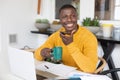 Smiling african american man using laptop at home, talking on smartphone and drinking coffee Royalty Free Stock Photo