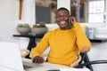 Smiling african american man using laptop at home and talking on smartphone Royalty Free Stock Photo