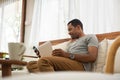 Smiling African American man using smartphone while sitting on sofa at home. Black Male Freelancer texting on mobile phone in Royalty Free Stock Photo