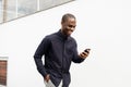 Smiling African American man walking with cellphone by white wall Royalty Free Stock Photo