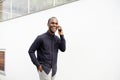 Smiling African American man walking with mobile phone by white wall Royalty Free Stock Photo