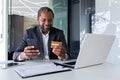 Smiling african american man working in office at desk, holding credit card and using mobile phone Royalty Free Stock Photo