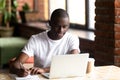 Smiling black male studying on laptop making notes in notebook