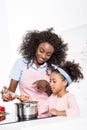 smiling african american mother and daughter putting ingredientes in saucepan