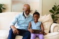 Smiling african american senior man with granddaughter using digital tablet while sitting on sofa Royalty Free Stock Photo