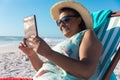 Smiling african american senior woman using digital tablet while sitting on folding chair at beach Royalty Free Stock Photo