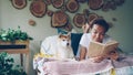 Smiling African American student lovely girl is reading book on bed at home while her pet dog is lying near her. Hobby Royalty Free Stock Photo