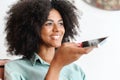 Smiling African-american woman with curly hair holding phone and speaking on speakerphone Royalty Free Stock Photo