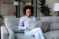 Smiling African American woman using laptop, relaxing on cozy couch Royalty Free Stock Photo